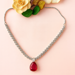 Necklace with a red teardrop pendant on a mannequin bust with flowers in the background