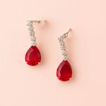 Pair of red teardrop earrings with american diamond accents on a pink background