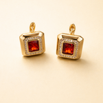 Gold tone earrings with red gemstones on a beige background