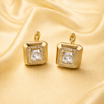 Gold tone earrings with clear gemstones on a gold satin background