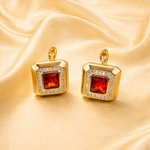 Gold tone earrings with red gemstones on a gold fabric background
