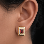 Gold tone earring with a red gemstone worn on an ear
