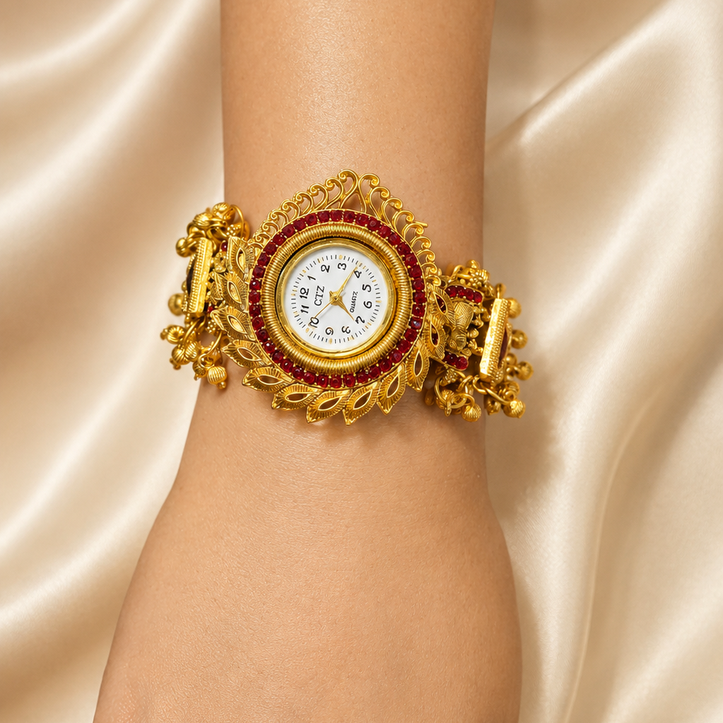 A close-up of a person's wrist wearing an ornate gold cuff watch with a white dial and a red gemstone border, set against a draped champagne satin background.