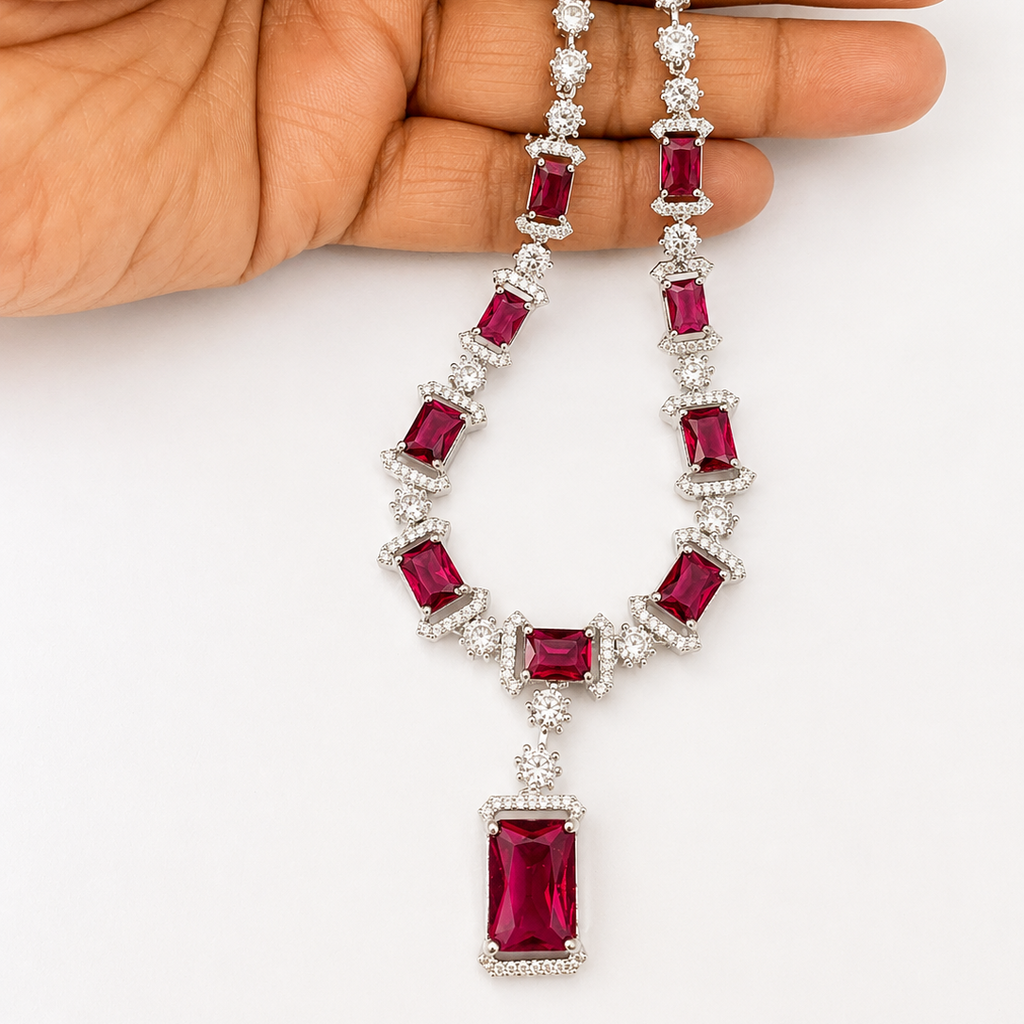 Ruby and diamond necklace held by a hand on a white background