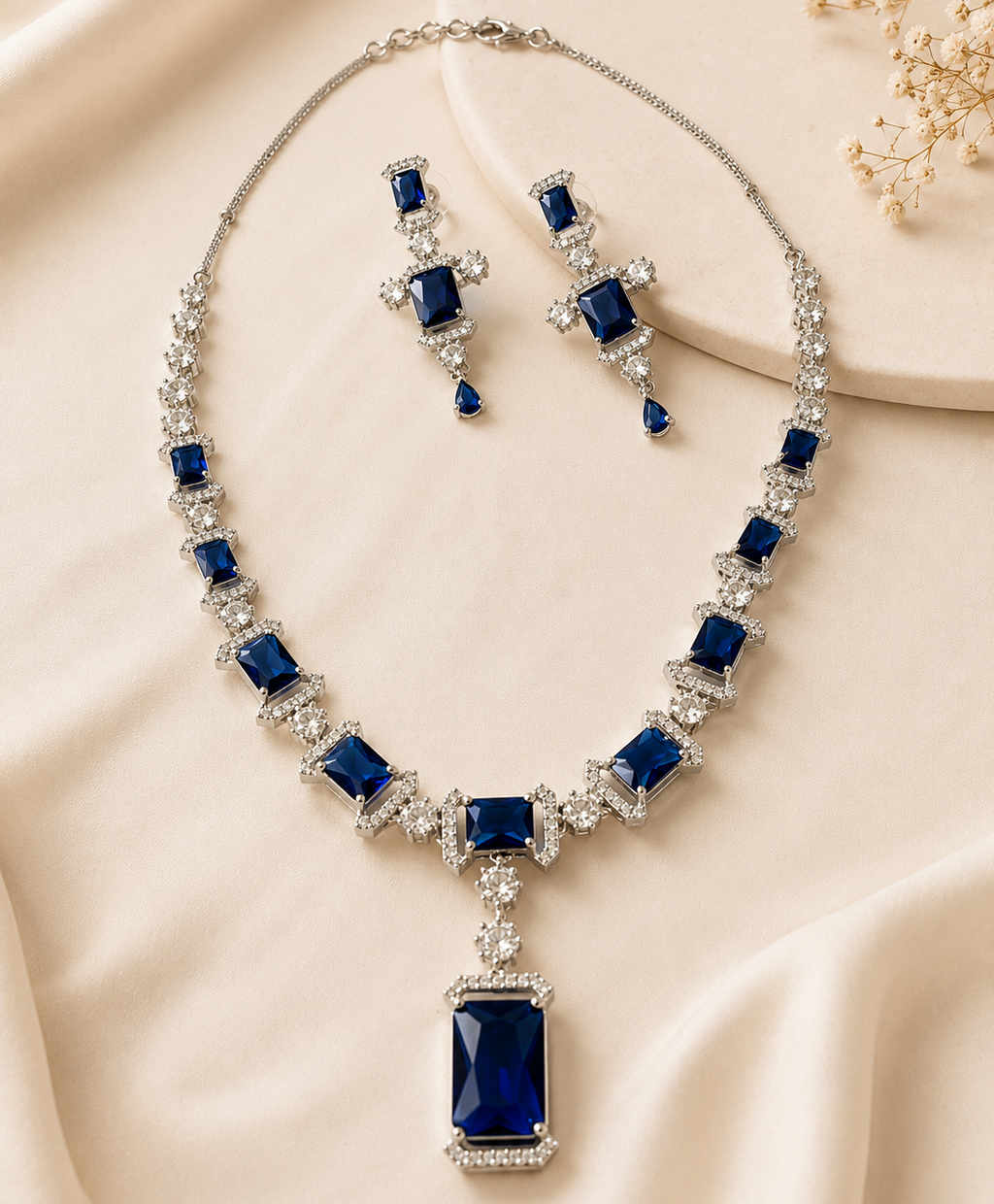 Jewelry set with necklace and earrings featuring blue gemstones on a beige fabric background