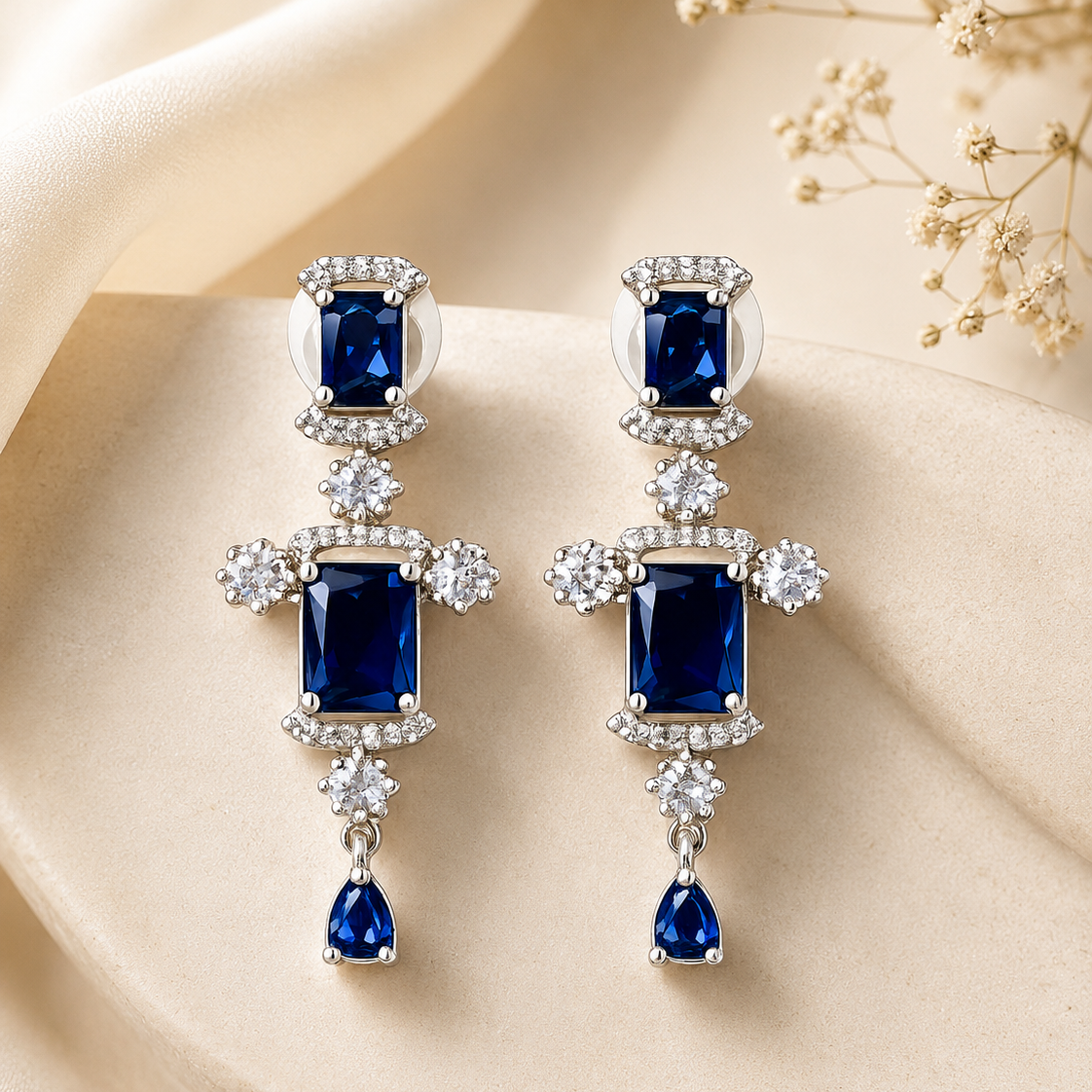 Pair of earrings with blue gemstones and diamond accents on a beige fabric background