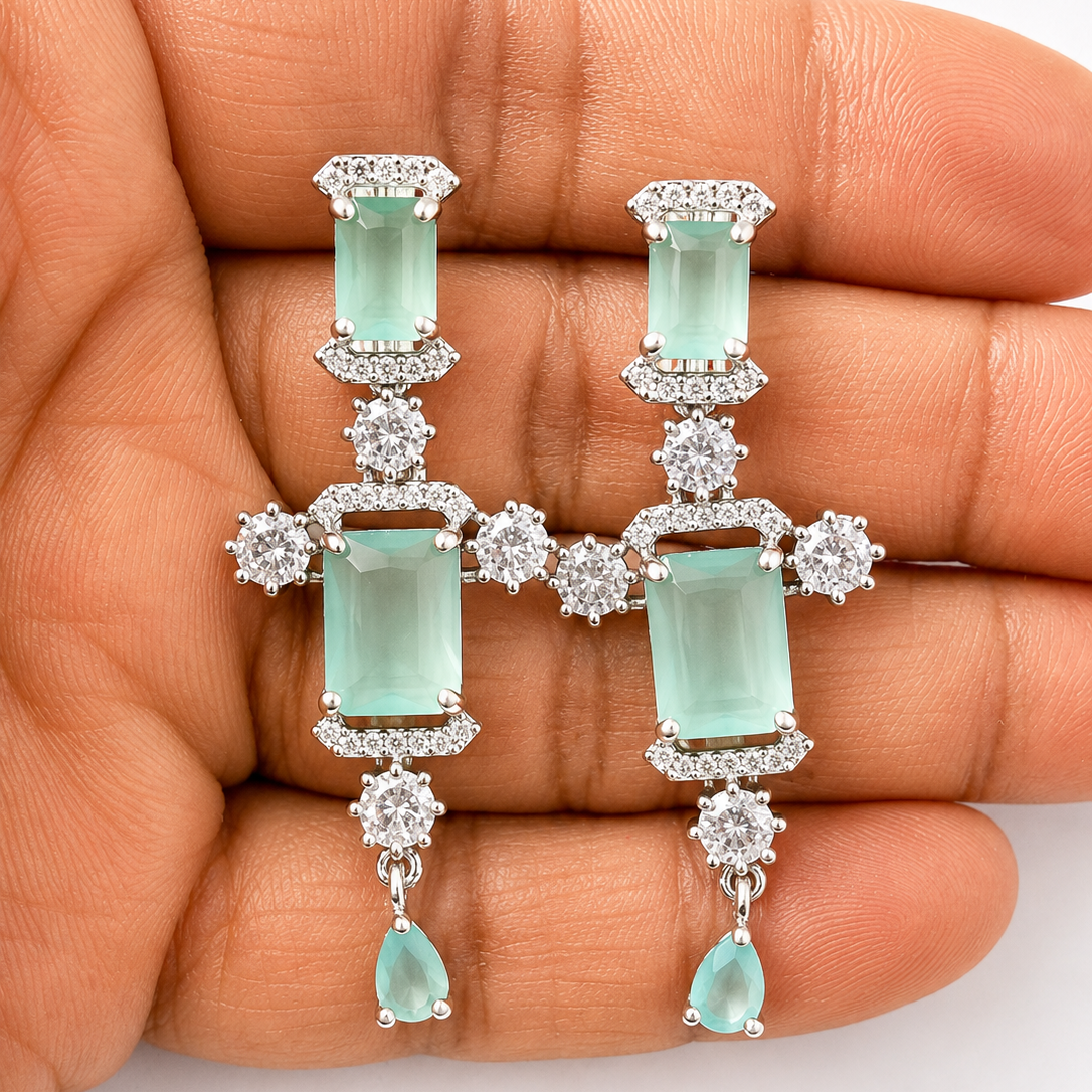 Aquamarine and diamond earrings held in a hand against a white background