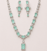 Jewelry set with necklace and earrings featuring green gemstones on a light pink background