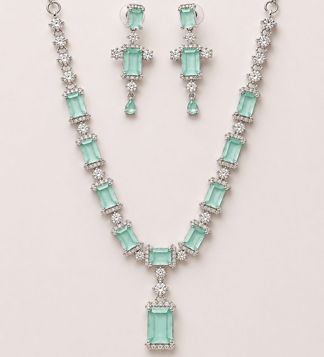Jewelry set with necklace and earrings featuring green gemstones on a light pink background