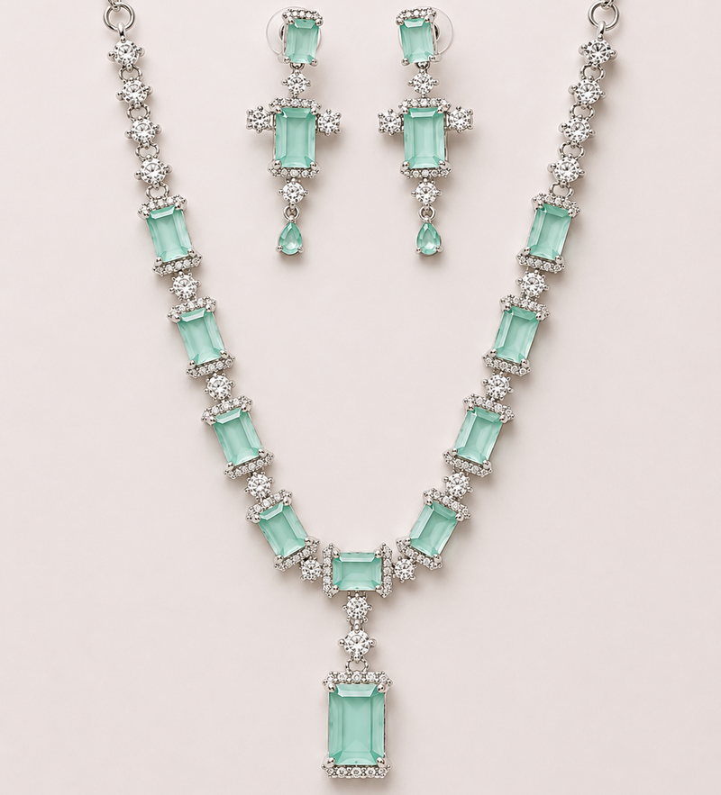 Jewelry set with necklace and earrings featuring green gemstones on a light pink background
