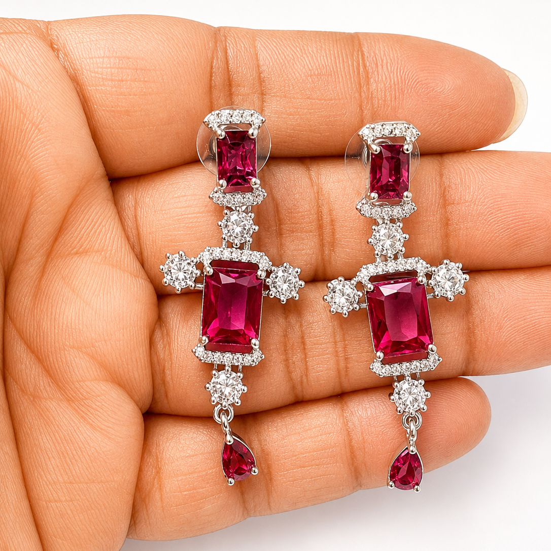 Pair of red gemstone earrings held in a hand against a white background