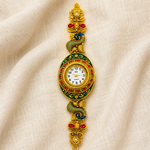 A decorative gold-plated wristwatch with a circular dial, surrounded by red and green enamel details, and a matching ornate link bracelet featuring a green-and-gold peacock motif, displayed on a draped beige fabric background.