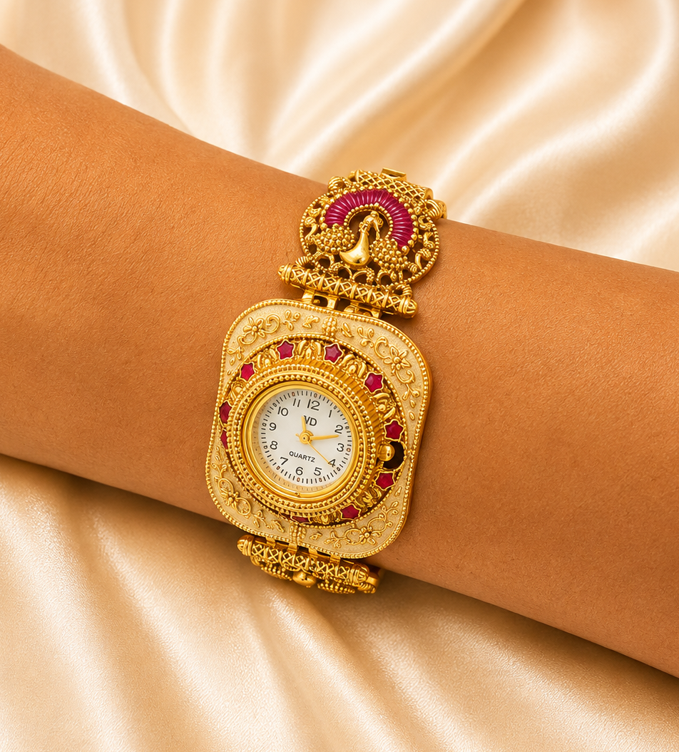 A close-up of a person's wrist wearing a traditional Indian gold-plated watch with a decorative dial, pink stone accents, and a peacock motif on the band, set against a draped champagne satin background.