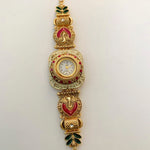 An ornate gold-plated watch bracelet featuring red and green enamel details, a central round watch face, and decorative motifs on a plain white background.
