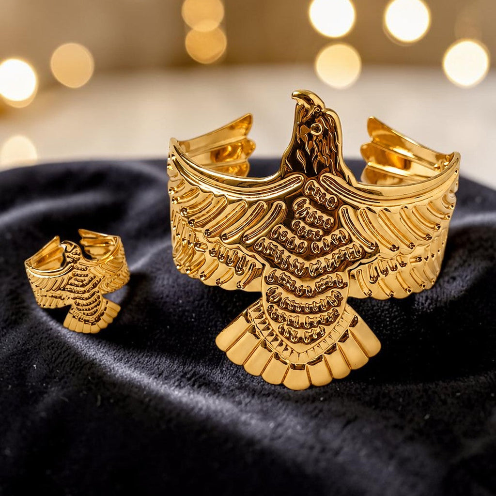 Gold tone eagle-shaped cufflinks on a black fabric background with blurred lights in the background