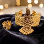 Gold tone eagle-shaped cufflinks on a black fabric background with blurred lights in the background