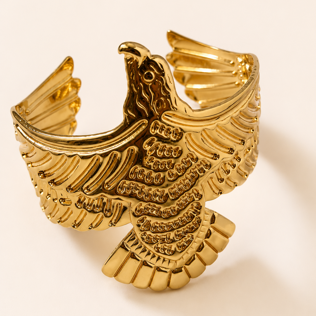 Gold tone eagle-shaped cuff bracelet on a light beige background