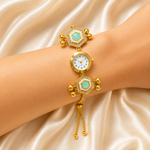 A gold-plated multi-link bracelet watch with turquoise inlay and crystal accents, shown worn on a wrist against a draped champagne satin background.