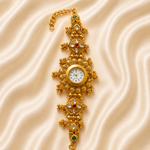 An ornate gold-toned wristwatch with intricate filigree detailing, small green and red gemstone accents, and a white dial, displayed on a beige satin fabric background.