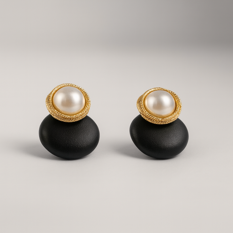 Pair of earrings with gold rims and pearl centers on black bases against a light gray background