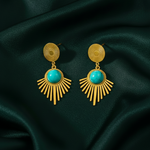 Gold earrings with turquoise stones on a dark green fabric background