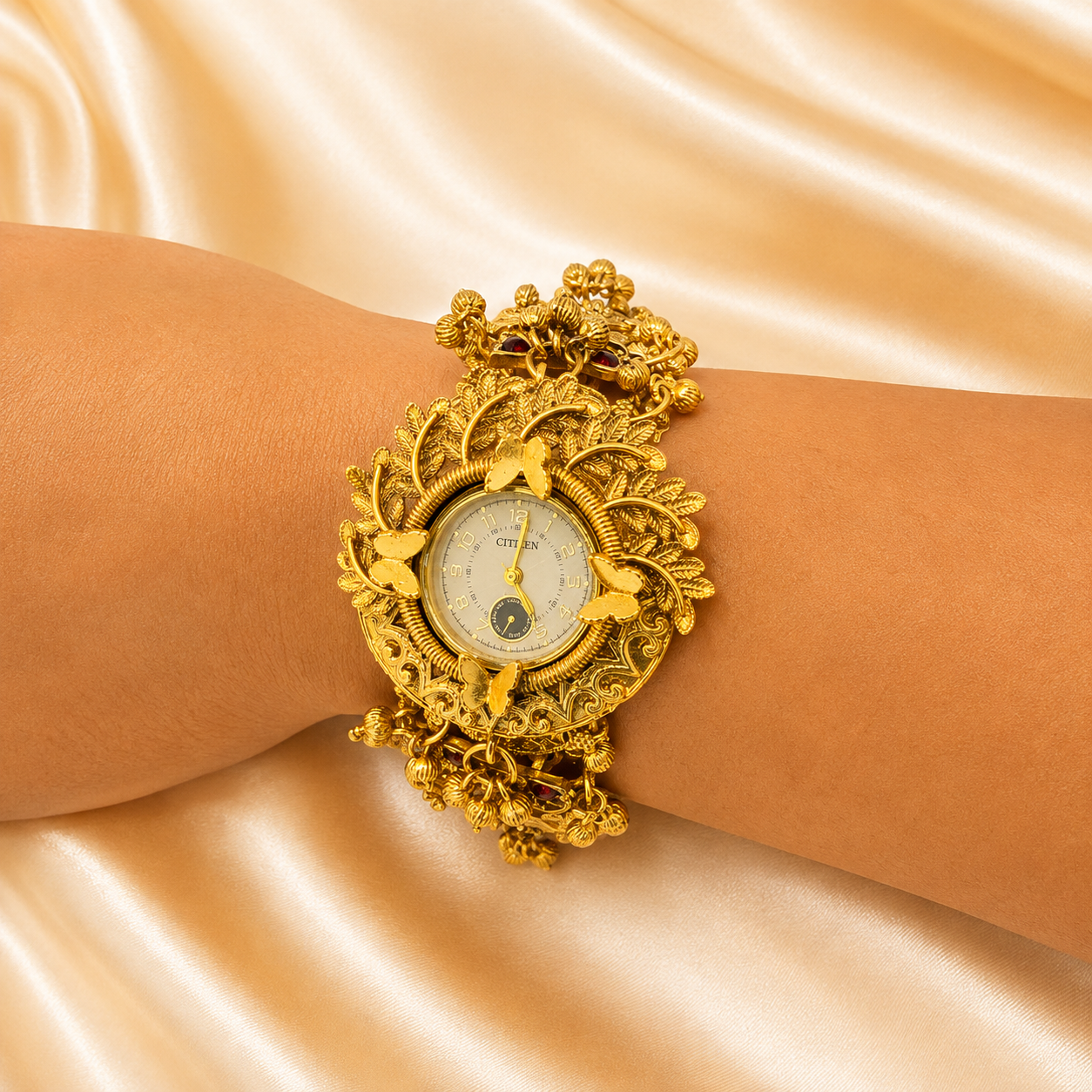 An ornate gold-tone watch with a wide, sculptural bracelet featuring floral and leaf motifs, worn on a wrist against a draped champagne satin background.