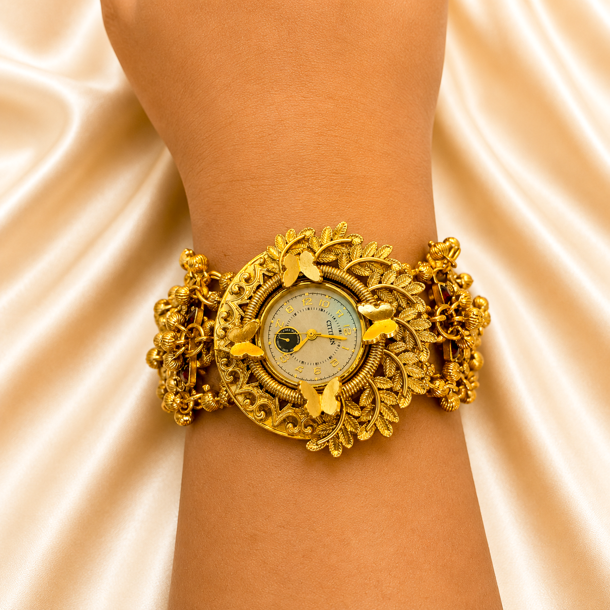 A gold-toned ornate wristwatch with butterfly and leaf filigree details, shown worn on a person's wrist against a draped satin fabric background.