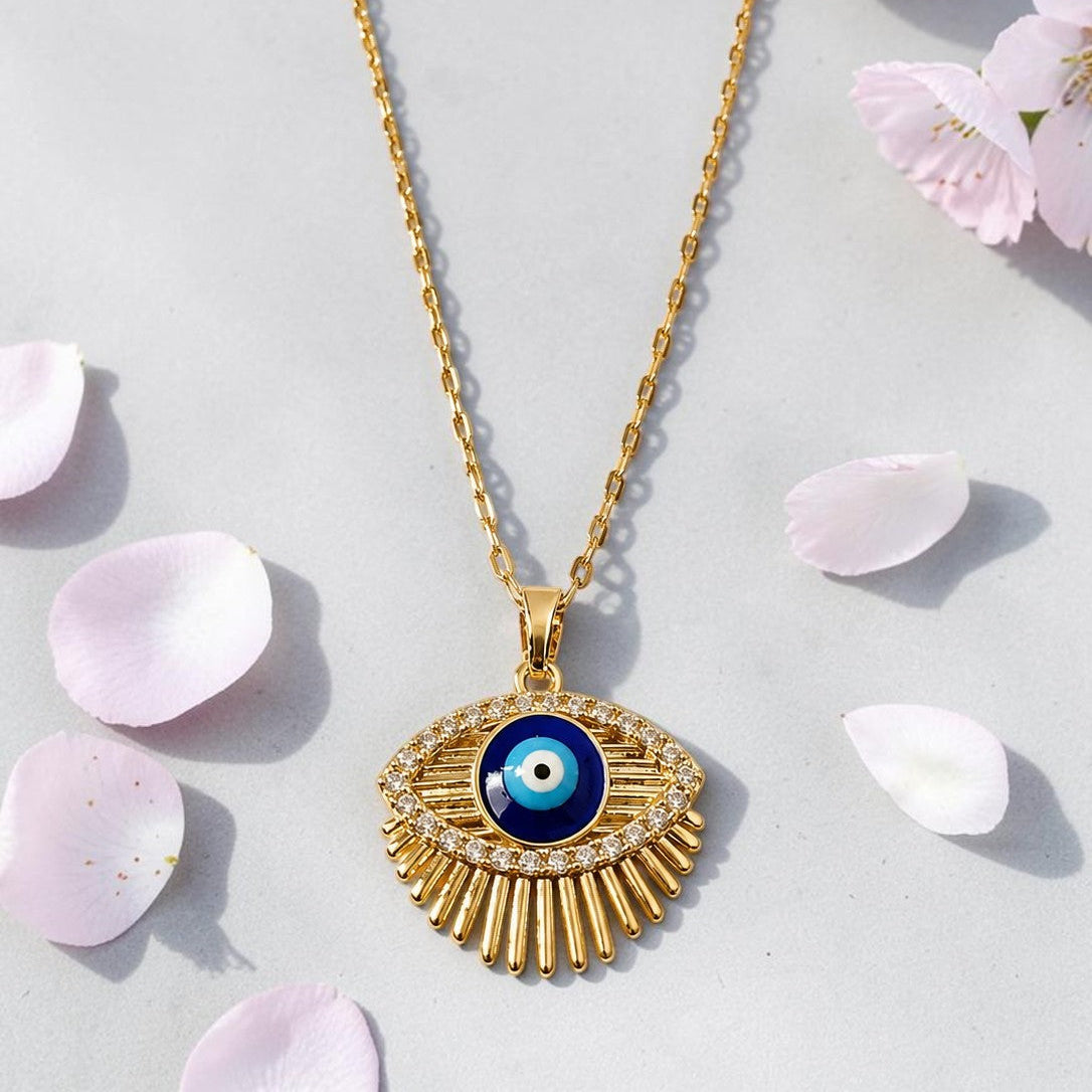 Gold tone necklace with an eye-shaped pendant on a light gray background with pink petals.
