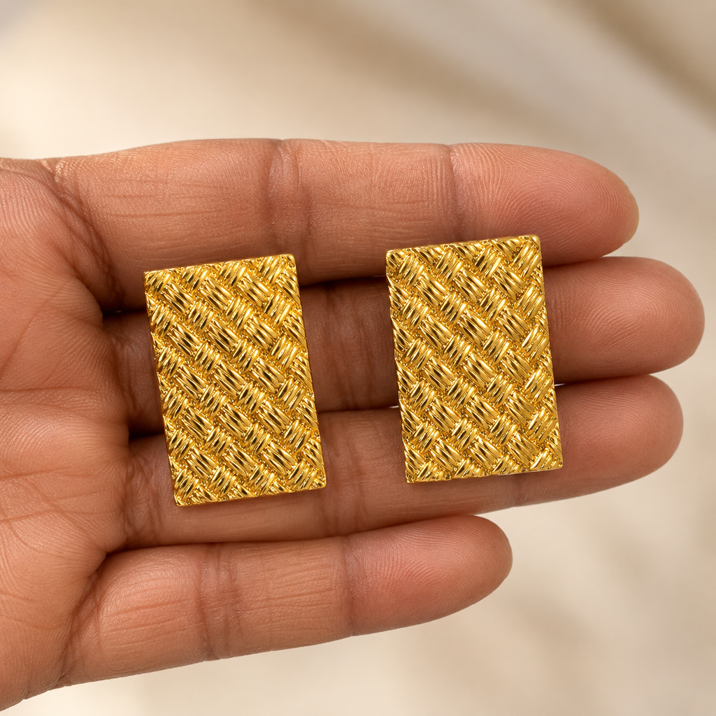 Gold textured square earrings held in a hand against a neutral background