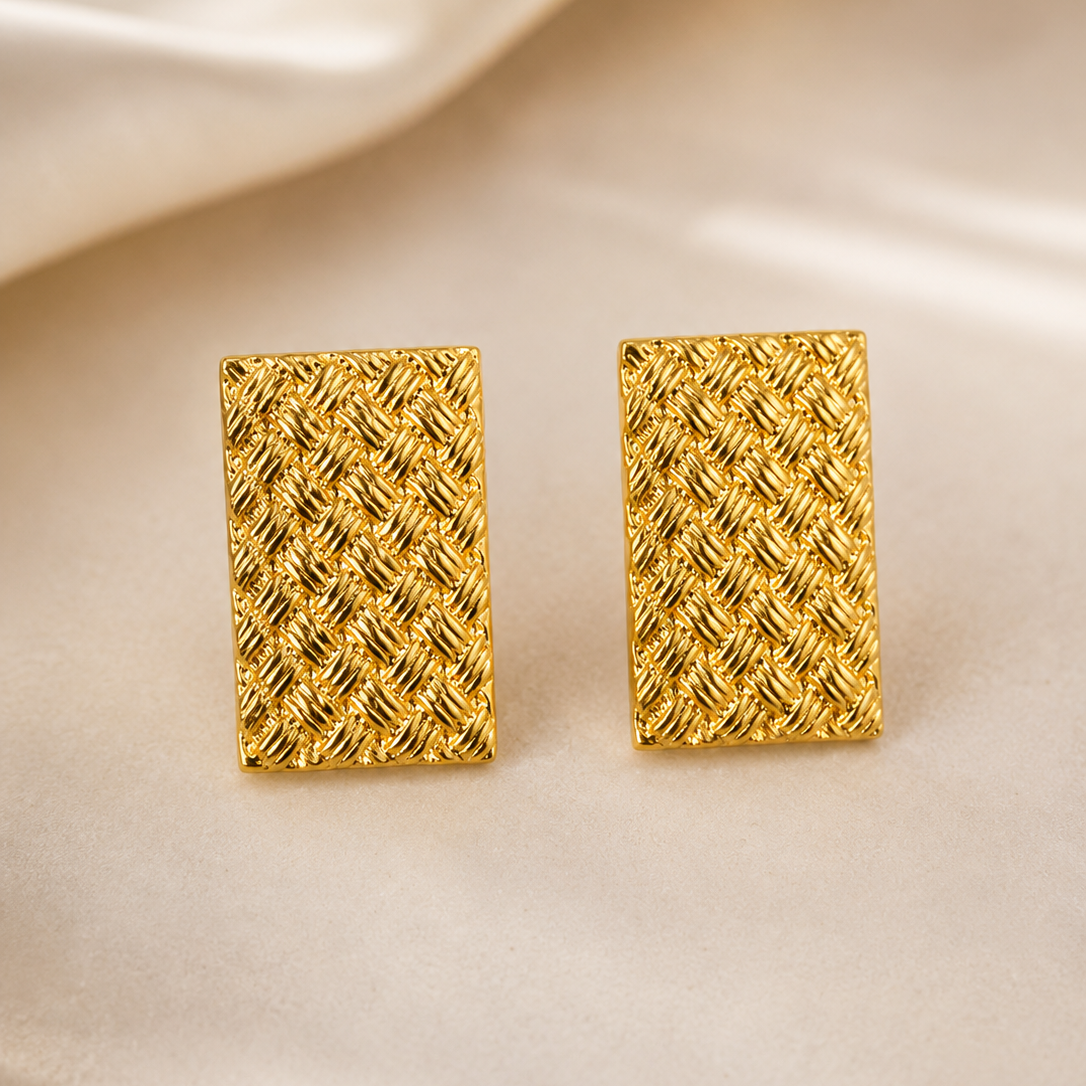 Pair of golden rectangular earrings on a beige fabric background
