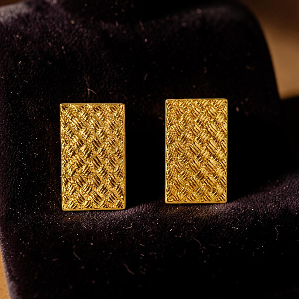 Pair of golden rectangular earrings on a black velvet background