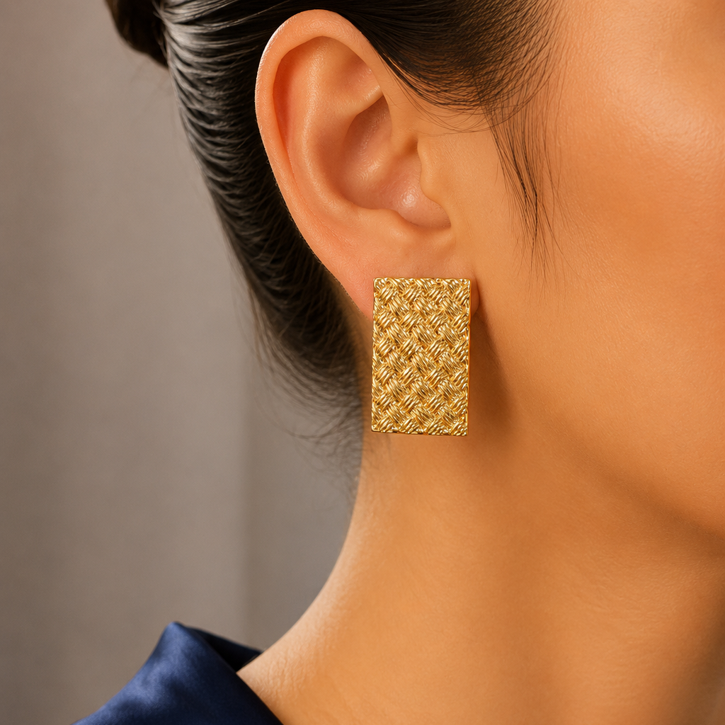 Gold textured earring worn by a person with a neutral background